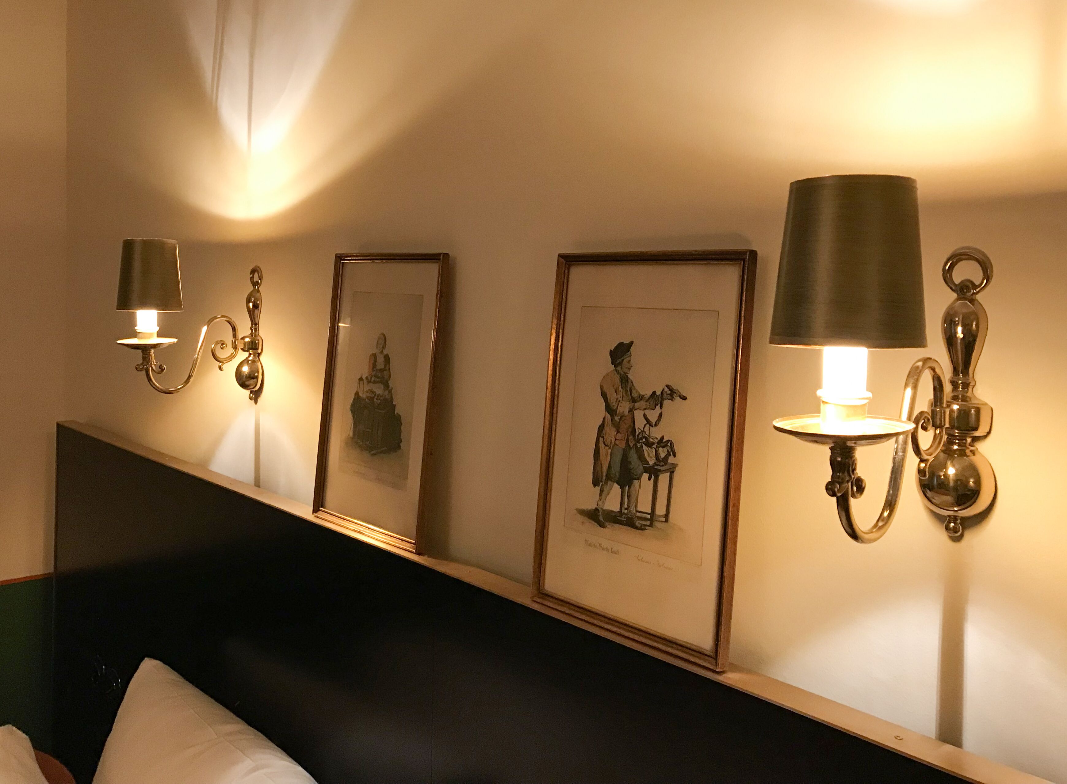 A hotel room with a bed, a headboard, and wall-mounted sconces with lamps.