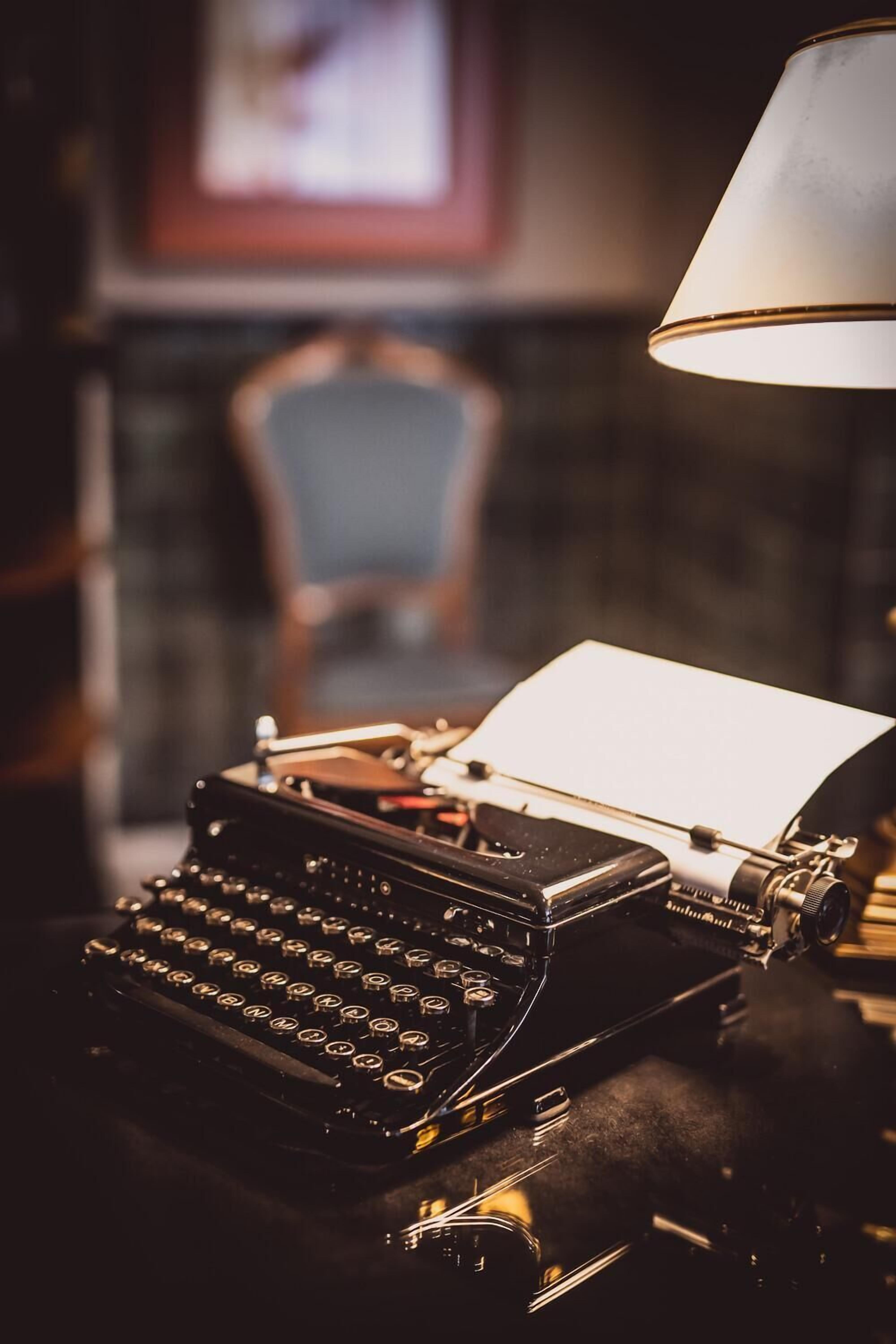 A vintage typewriter on a desk with a lamp, in a room with a blurred background.