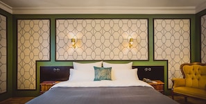 Quarto de hotel com uma cama grande, duas mesas de cabeceira, um criado-mudo, uma cadeira e um painel decorativo na parede com duas luzes.