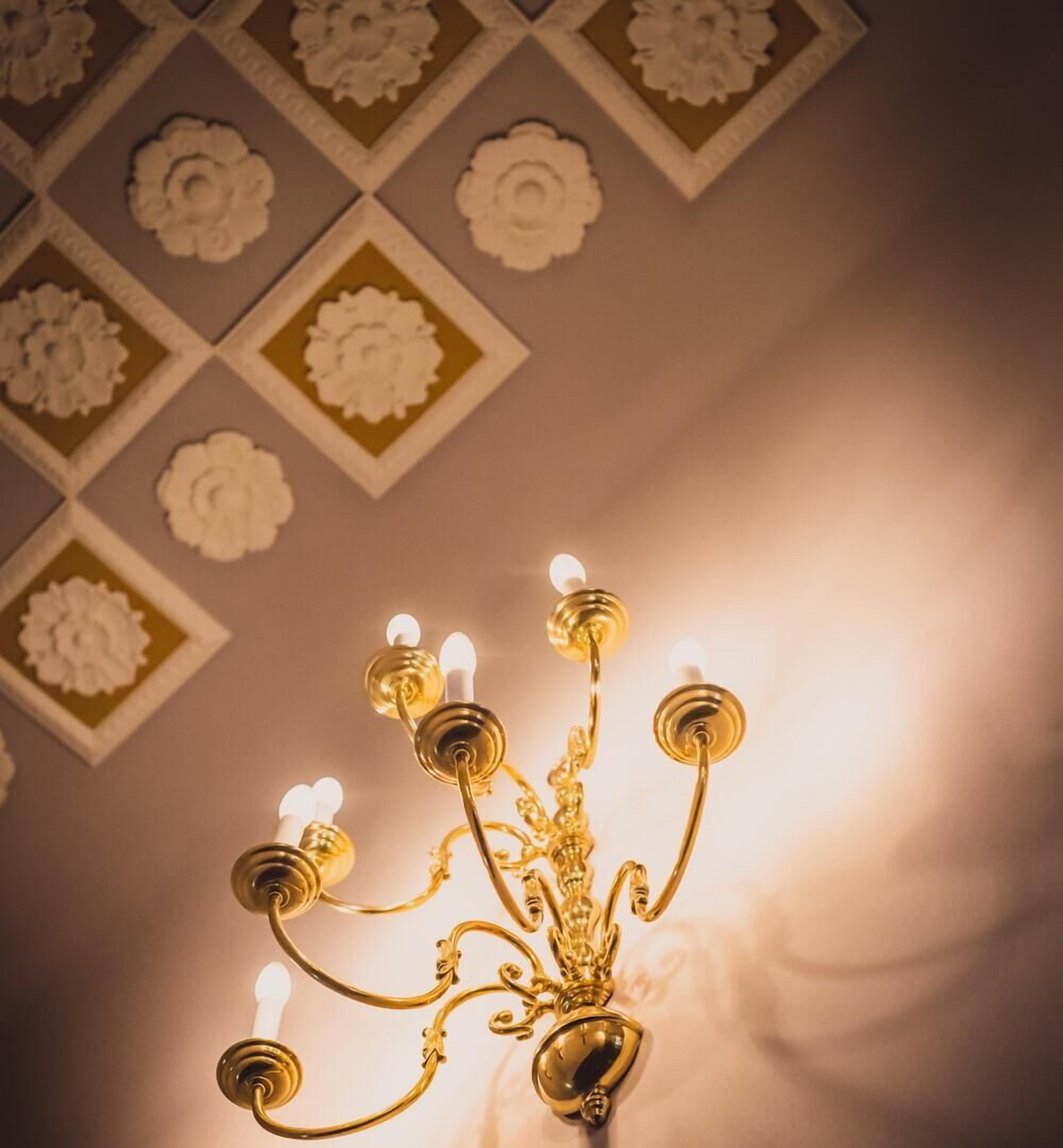 Un lustre à plusieurs bras et à plusieurs ampoules, placé sur un mur orné d’un motif floral géométrique.
