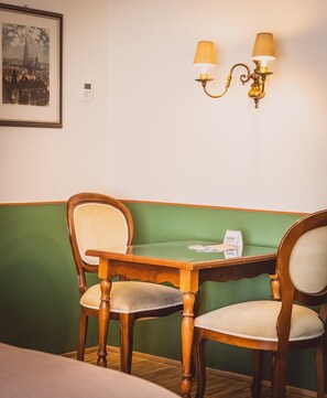 A room with a green cushioned bench, two wooden chairs, a wooden table, and a wall-mounted lamp. - HENRI Hotel Wien (Vienna)