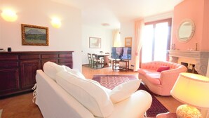 A living room with a white sofa, a pink armchair, a fireplace, and a television. - Pognana Luxury Apartment n.1 - 7 people (Pognana Lario)