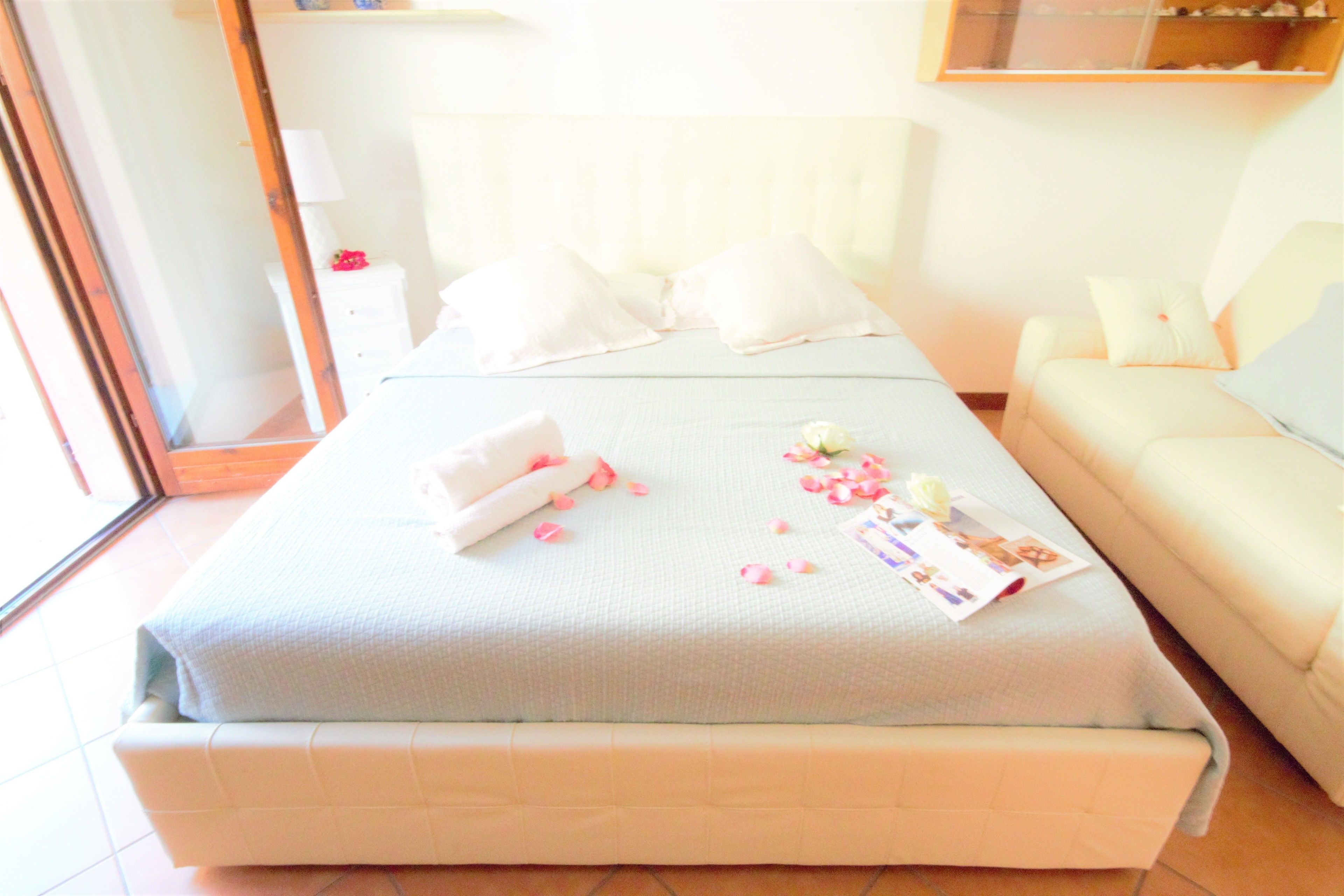 A neatly made bed with pillows, a bedside table with a lamp, and a sofa with cushions.
