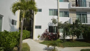A modern building with multiple balconies, a paved walkway, and various plants.