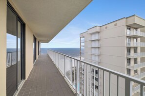 Un balcón con vista al mar, suelo de baldosas y un edificio con varios balcones.