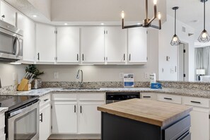 A modern kitchen with white cabinetry, a granite countertop, a built-in dishwasher, and a wooden island. - White Caps 1406 | Beachfront Orange Beach Condo | Wrap Balcony, Sleeps 10 (Orange Beach)