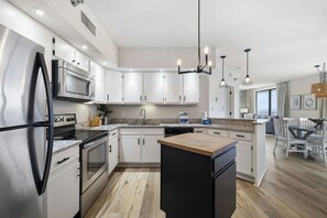 A modern kitchen with stainless steel appliances, white cabinetry, and a wooden island. - White Caps 1406 | Beachfront Orange Beach Condo | Wrap Balcony, Sleeps 10 (Orange Beach)