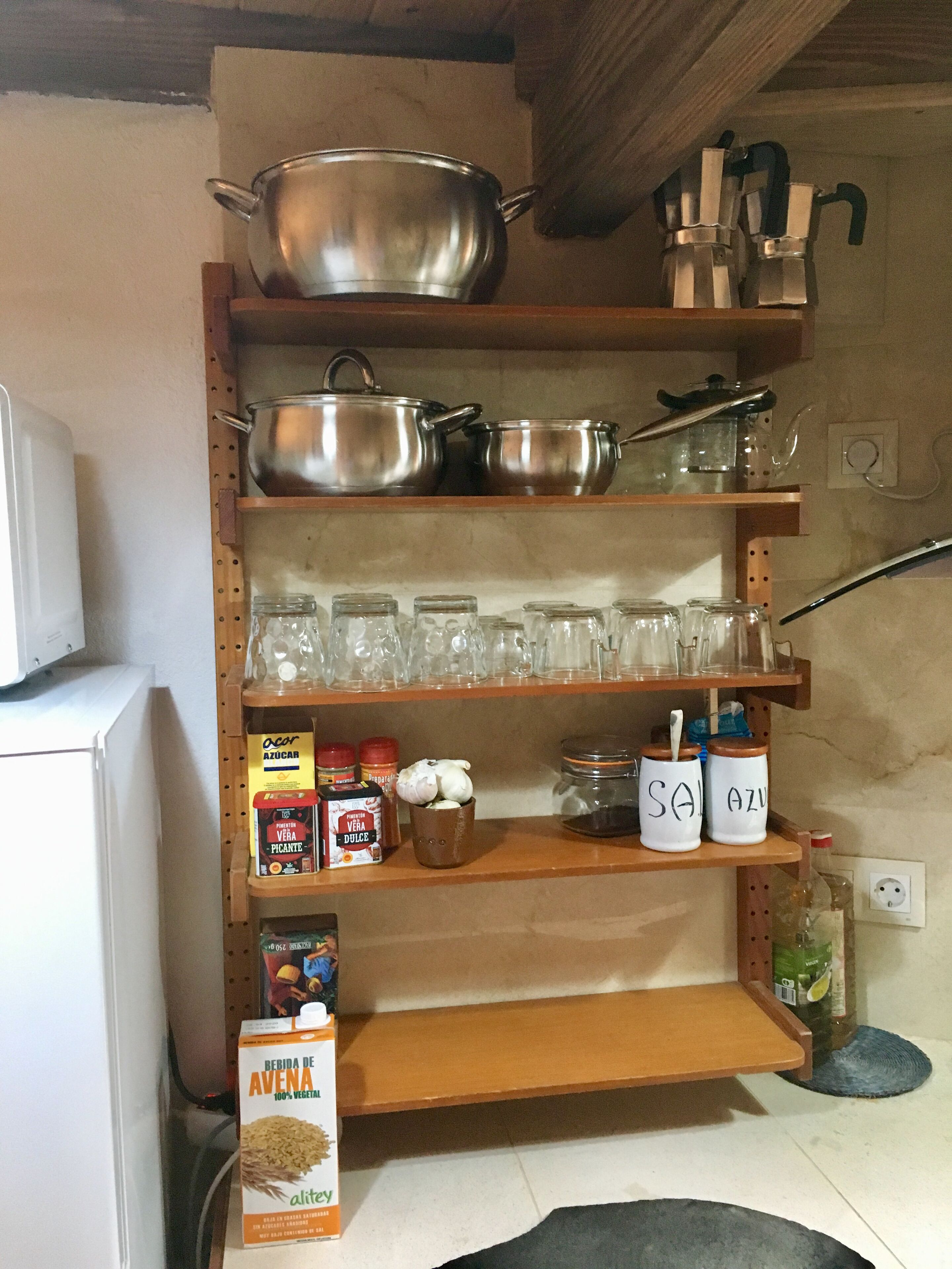 A kitchen with shelves holding pots, pans, glassware, and jars.