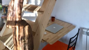 Una escalera de madera con acabado natural, un ordenador portátil sobre una estantería de madera y una silla roja.
