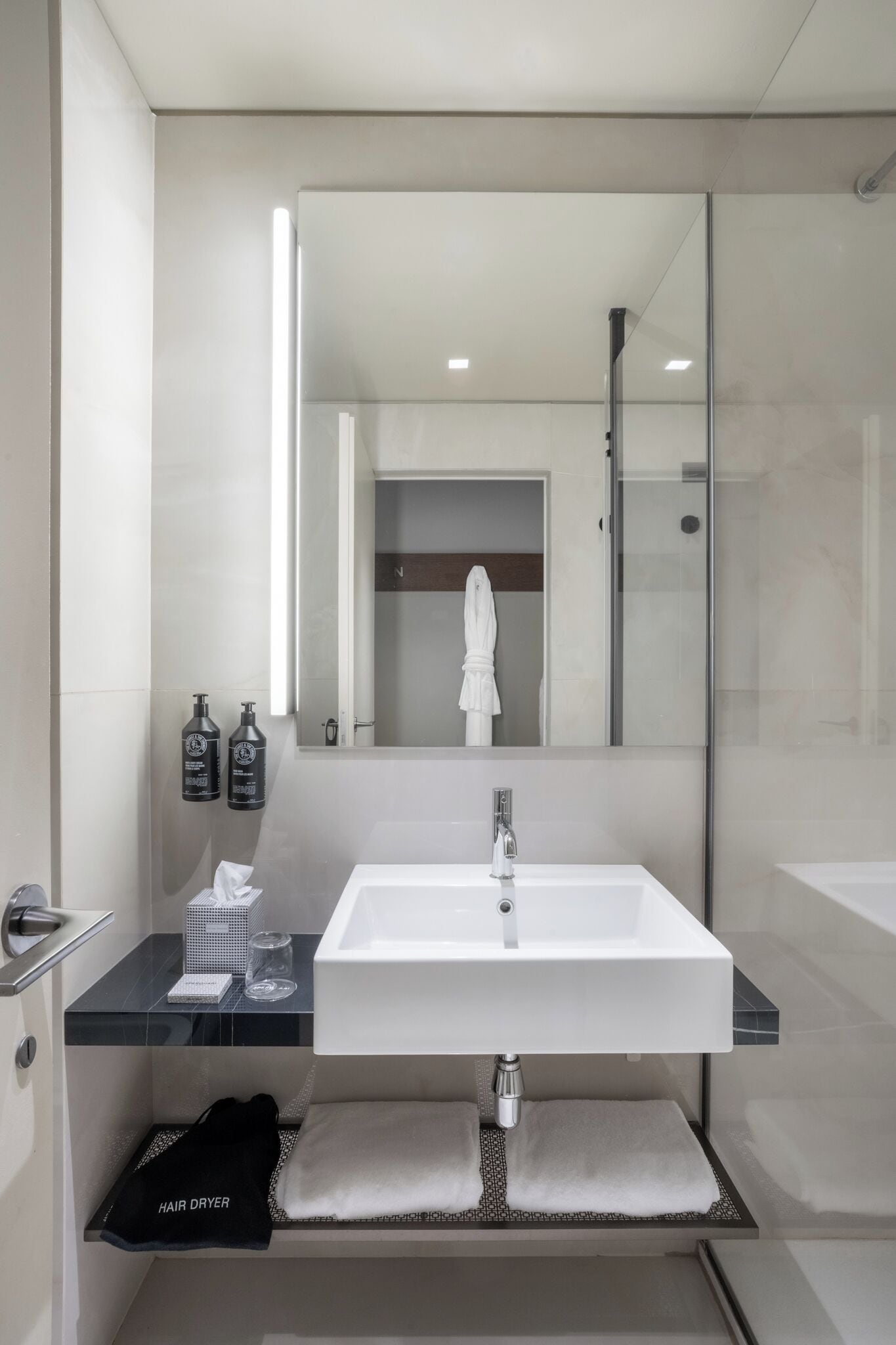 A modern bathroom with a large mirror, white sink, and a towel rack.