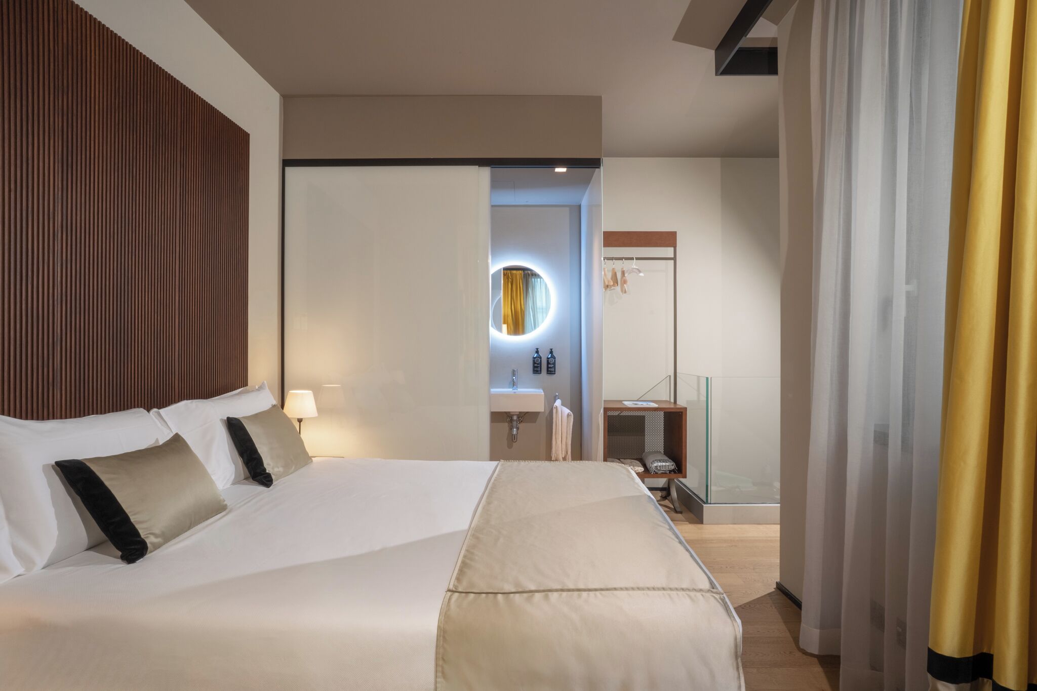 A hotel room with a large bed, a bedside table, a mirror, a bathroom with a sink, and a door with a curtain.
