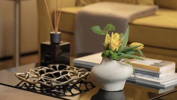 Una sala de estar moderna con una mesa de centro de vidrio, un jarrón con flores, una escultura metálica decorativa y un sofá con cojines.
