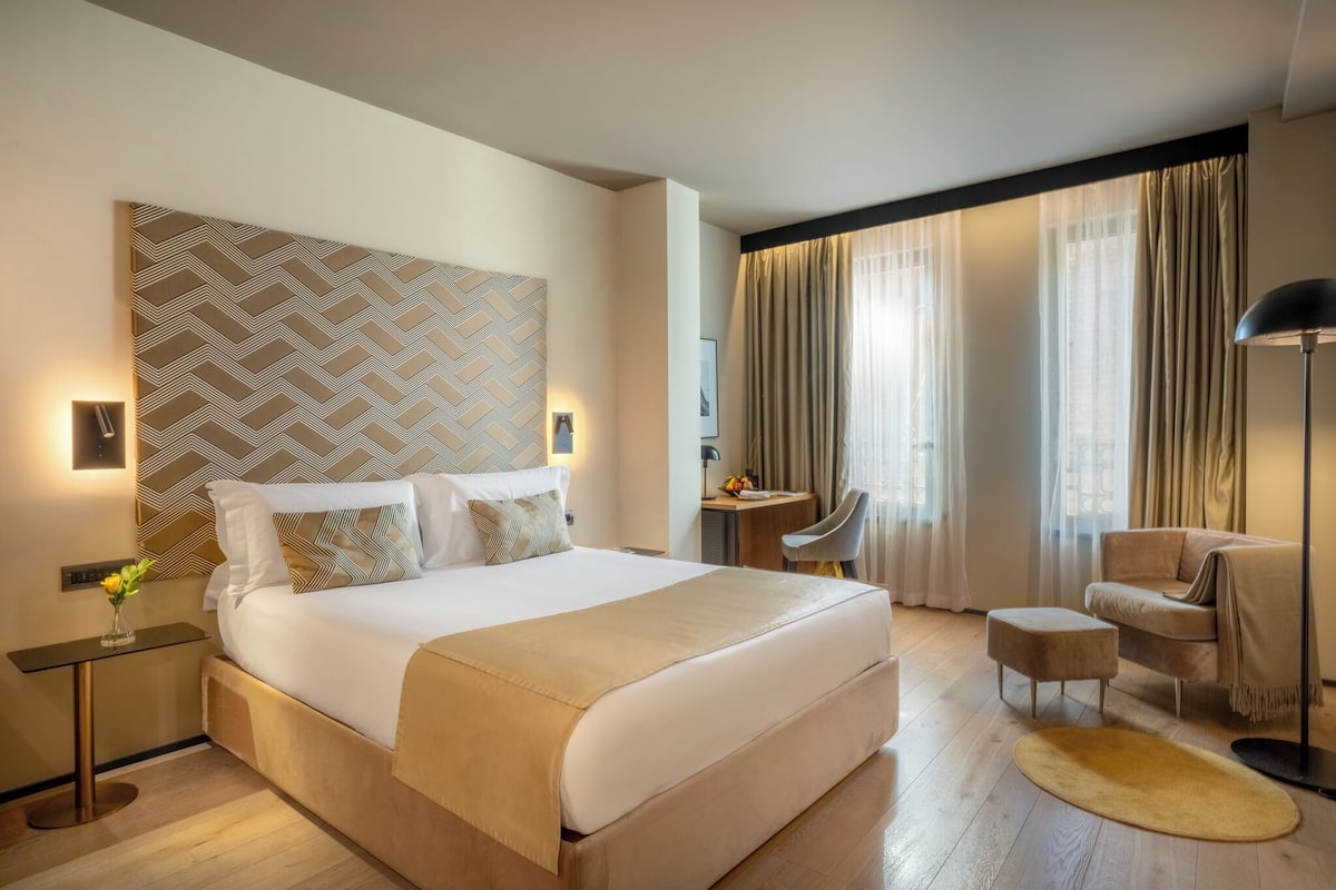 A hotel room with a large bed, a desk, a chair, and a sofa.