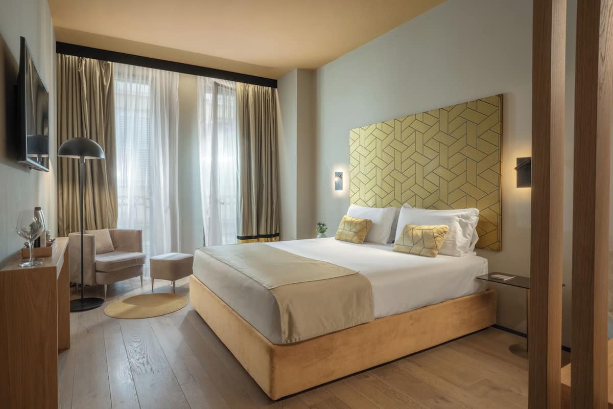 A modern hotel room with a large bed, a desk, a chair, and a TV.