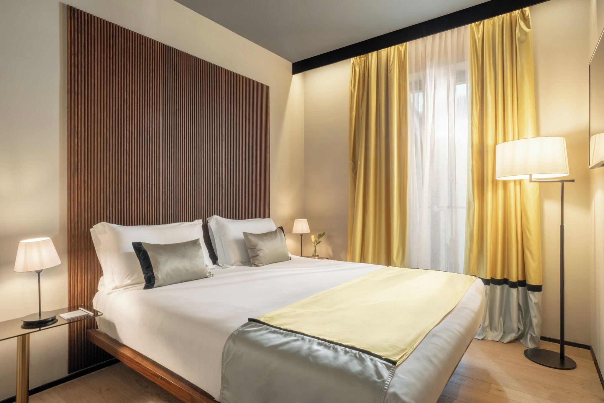 Une chambre d’hôtel avec un lit, des tables de chevet, une lampe et des rideaux.