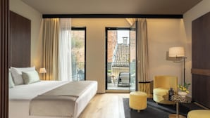 A hotel room with a bed, a sofa, a chair, a small table, and a balcony with a view of buildings. - Speronari Suites (Milan)