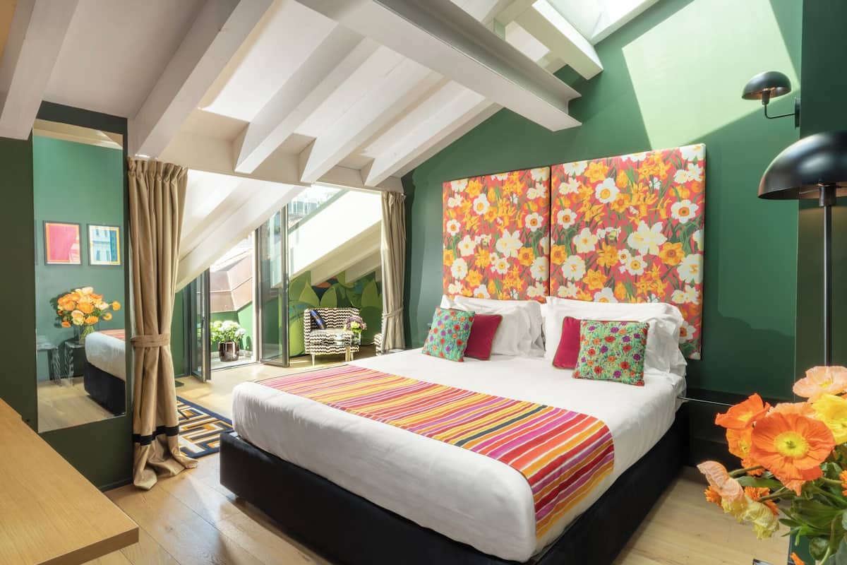 A bedroom with a large bed, a chair, a table, and a view of the outdoors.