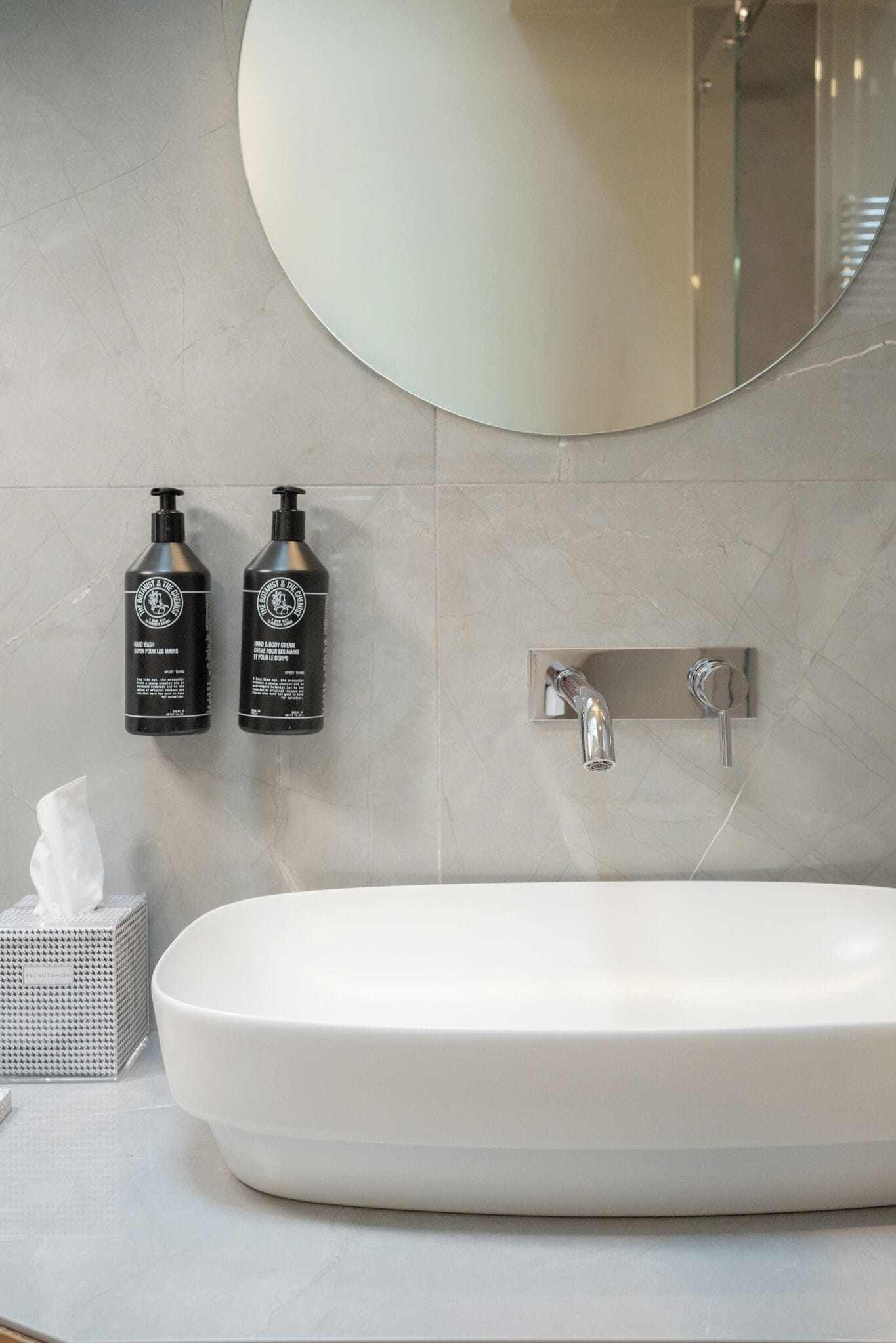 A bathroom with a white sink, two black bottles of shampoo, a mirror, and a towel dispenser.