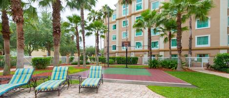 A courtyard with palm trees, a basketball court, and lounge chairs.