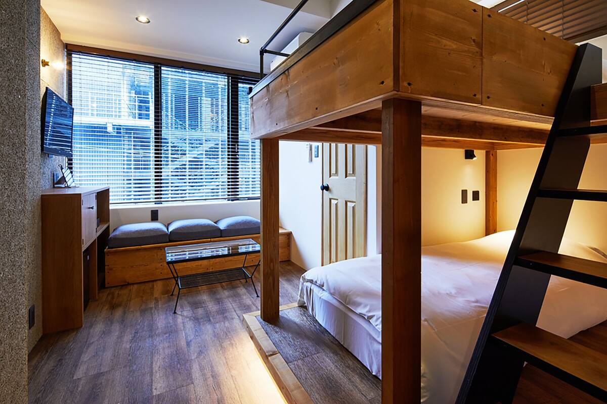 A bunk bed room with a desk and a window with blinds.