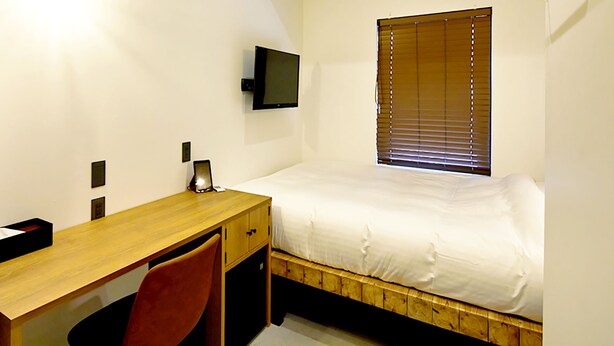 Ein Schlafzimmer mit einem hölzernen Bett, einem Schreibtisch, einem Stuhl, einem an der Wand befestigten Fernseher und einem Fenster mit Jalousien.