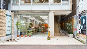 A modern building with a glass storefront, potted plants, and a staircase leading to an upper level. - mizuka Daimyo 6 - unmanned hotel - (Fukuoka)