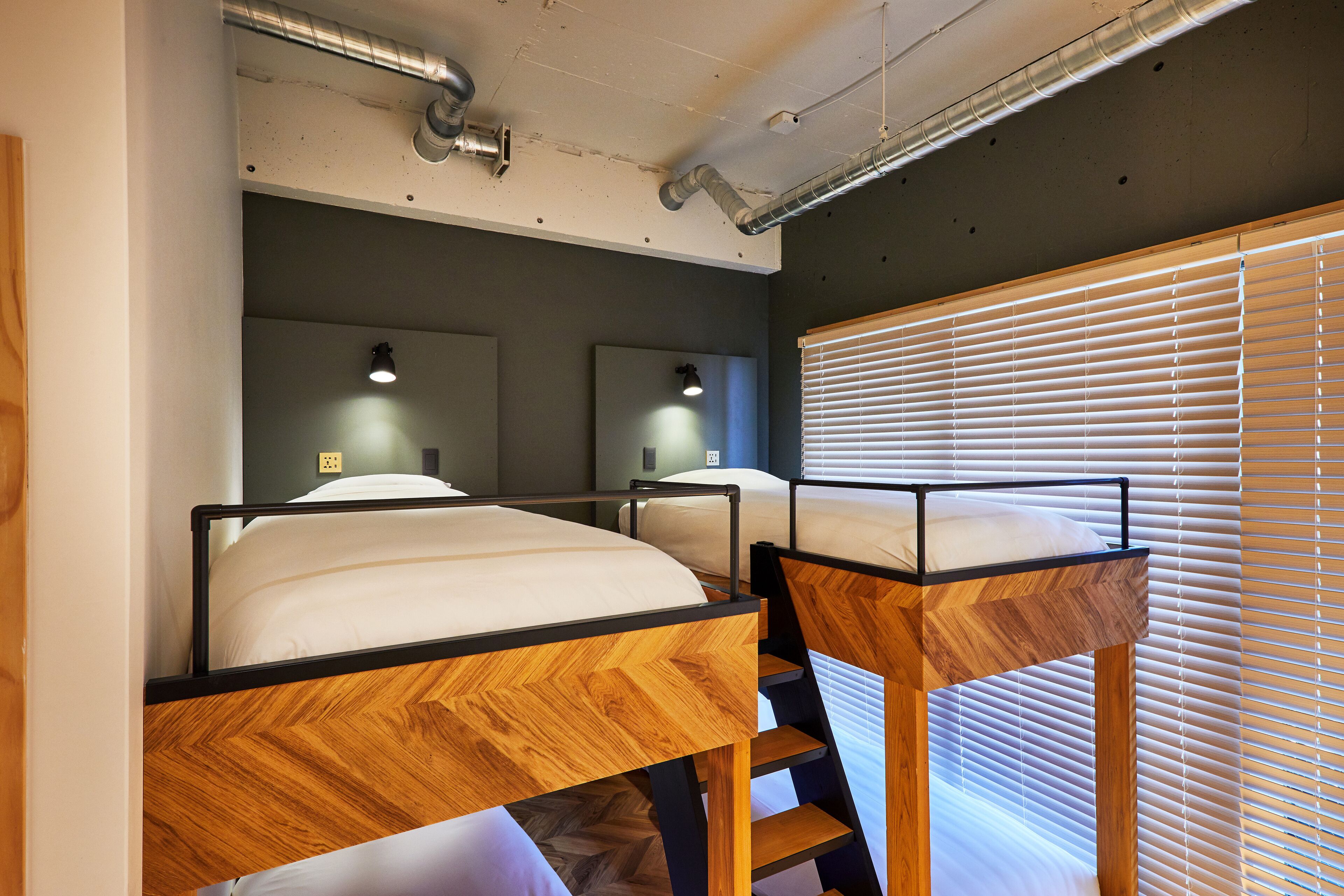 A room with bunk beds, wooden headboards, and a window with blinds.