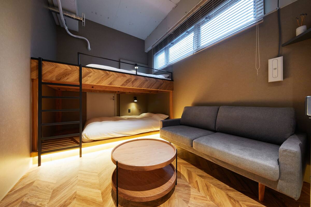 Une petite pièce comprenant un lit superposé, un canapé et une table ronde en bois.
