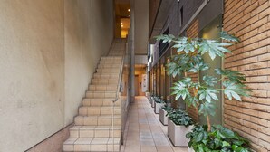 A narrow corridor with a staircase leading to an upper level, flanked by potted plants and a brick wall. - mizuka Daimyo 6 - unmanned hotel - (Fukuoka)