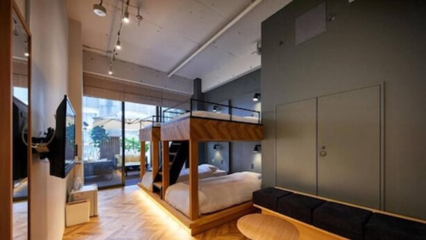 A modern hotel room with a bunk bed, a sofa, a round wooden table, and a large window offering a view of the outdoors. - mizuka Daimyo 6 - unmanned hotel - (Fukuoka)