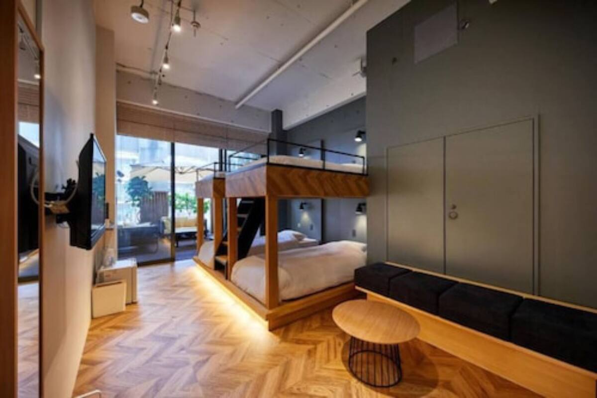 Une chambre d’hôtel moderne équipée d’un lit superposé, d’un canapé, d’une table ronde en bois et d’une grande fenêtre donnant sur l’extérieur.