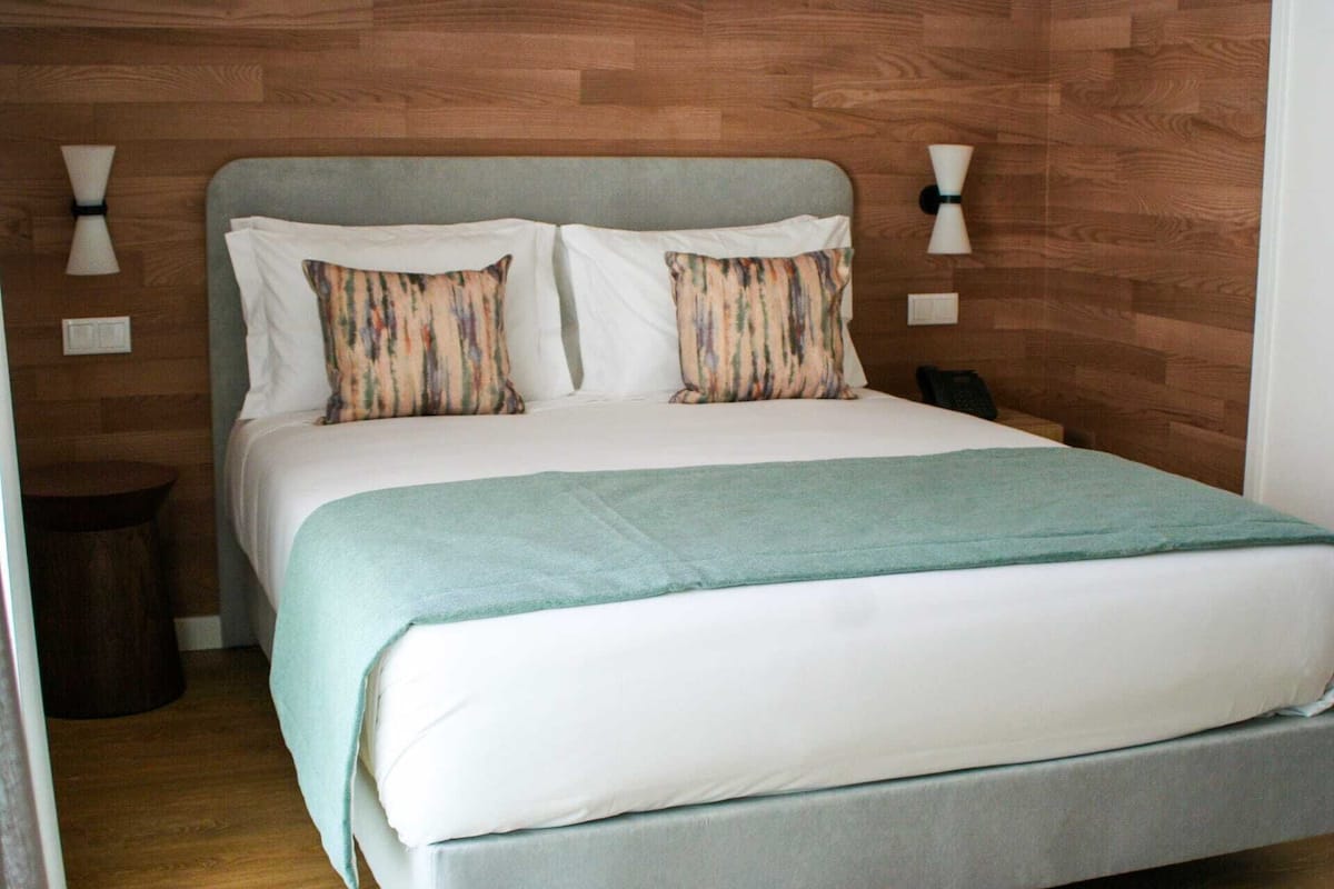 Una cama bien tendida con una colcha azul claro y dos almohadas a rayas.