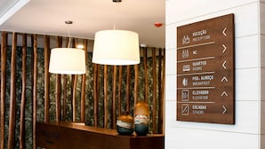 A reception desk with a wooden panel wall and a directional sign. - Cascais City Beach Hotel (Cascais)