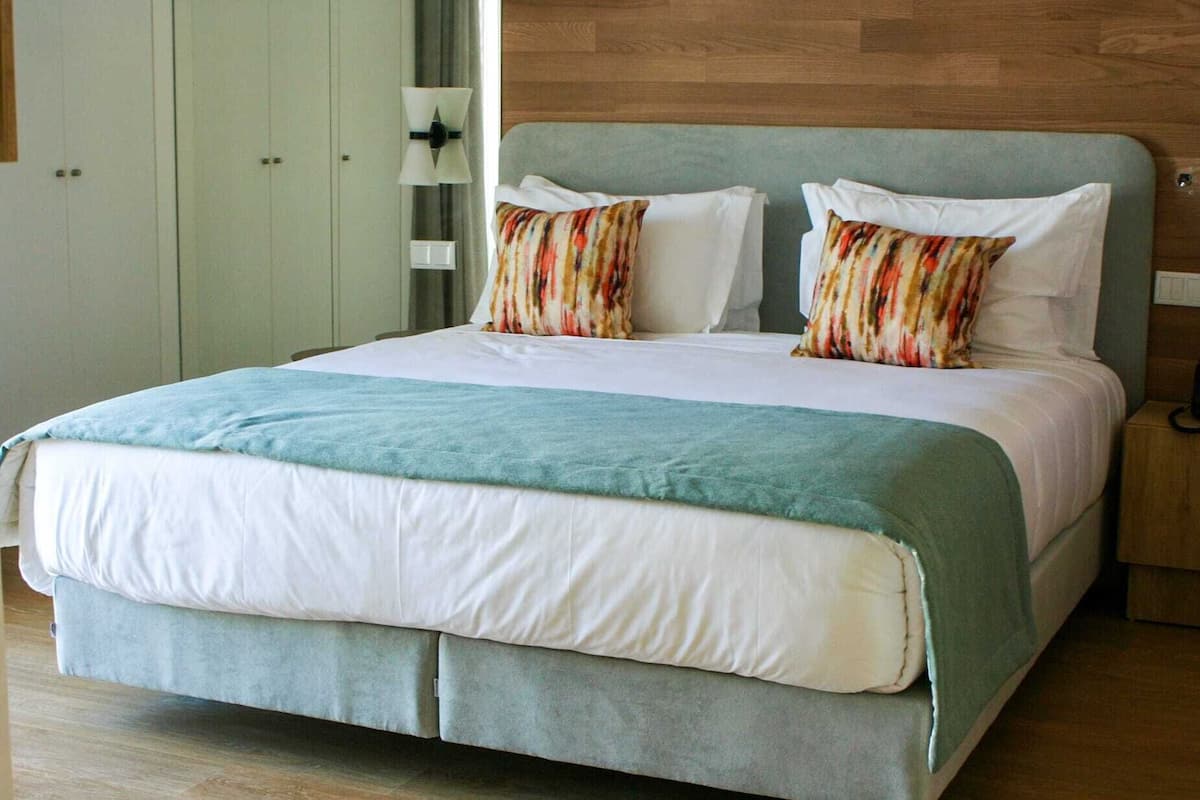 Una cama con edredón azul claro y blanco, dos almohadas estampadas a rayas y una manta azul claro a juego.