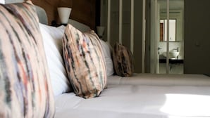 A bed with striped pillows, a bedside lamp, and a view of a bathroom with a sink and mirror. - Cascais City Beach Hotel (Cascais)