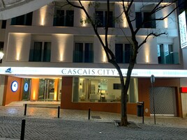 Un hotel llamado "CASCAIS CITY Beach Hotel" con una fachada moderna, grandes ventanales y una entrada visible.