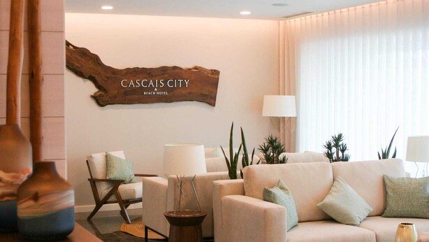 A modern living room with a sofa, armchairs, and a coffee table. A wooden sign reads "CASCAIS CITY & BEACH HOTEL". - Cascais City Beach Hotel (Cascais)