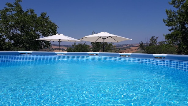 Une piscine à l’eau d’un bleu cristallin, entourée d’arbres et avec des collines en arrière-plan.