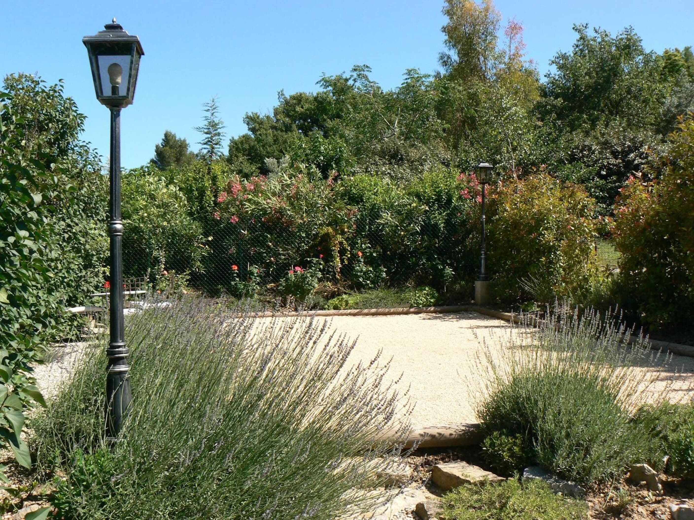 A garden pathway with a lamp post, surrounded by dense foliage and flowering plants.