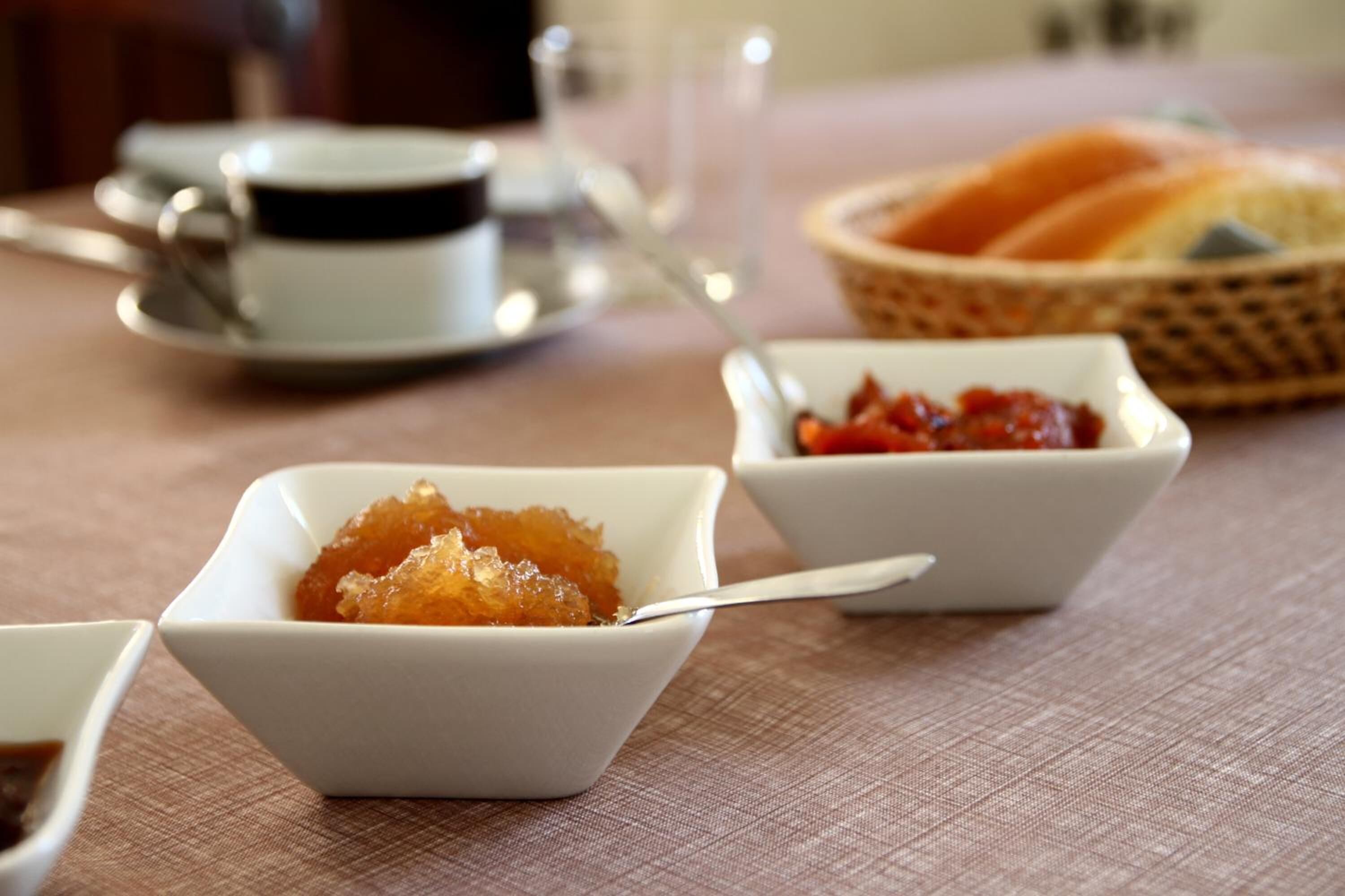 Een tafel met een witte kop, een schaaltje jam en een mand met brood.
