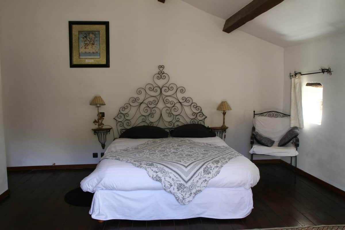 A bedroom with a large bed, two bedside tables with lamps, a chair, and a window with curtains.