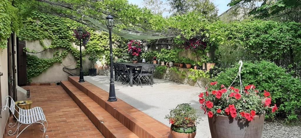 Un patio con mesa y sillas, rodeado de follaje y plantas en macetas.