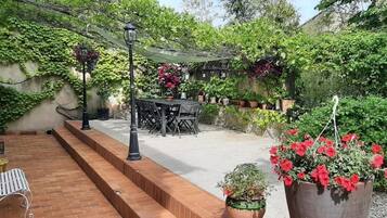 Un patio con mesa y sillas, rodeado de follaje y plantas en macetas.