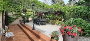 Un patio con mesa y sillas, rodeado de follaje y plantas en macetas.