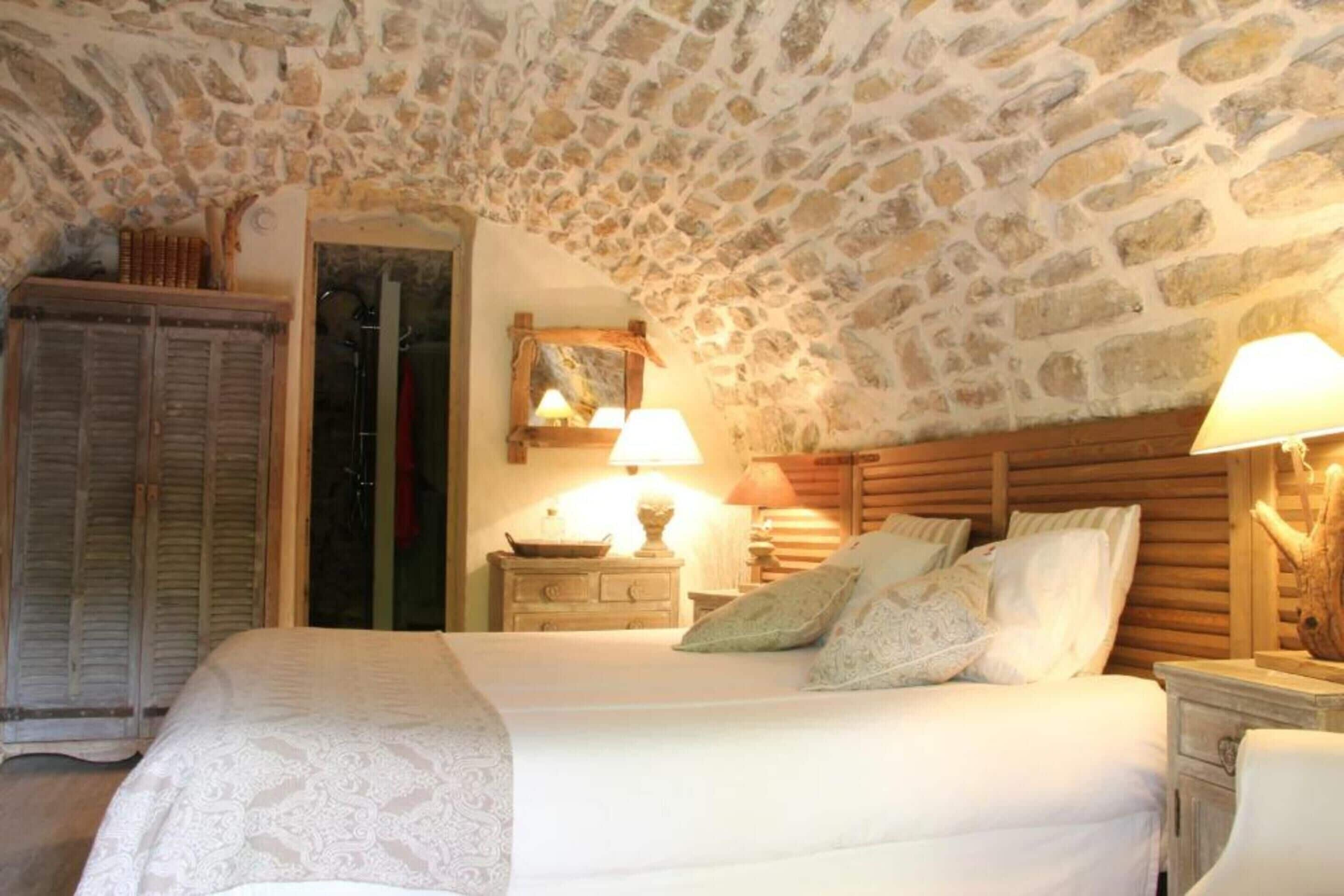 Quarto com teto de pedra, cabeceira de madeira e cama com roupa de cama branca.