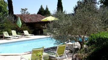 A pool area with lounge chairs and a building with a tiled roof.