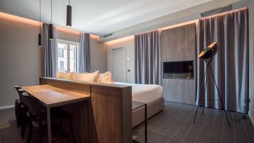A modern hotel room with a wooden desk, a bed, a TV, and a standing lamp.
