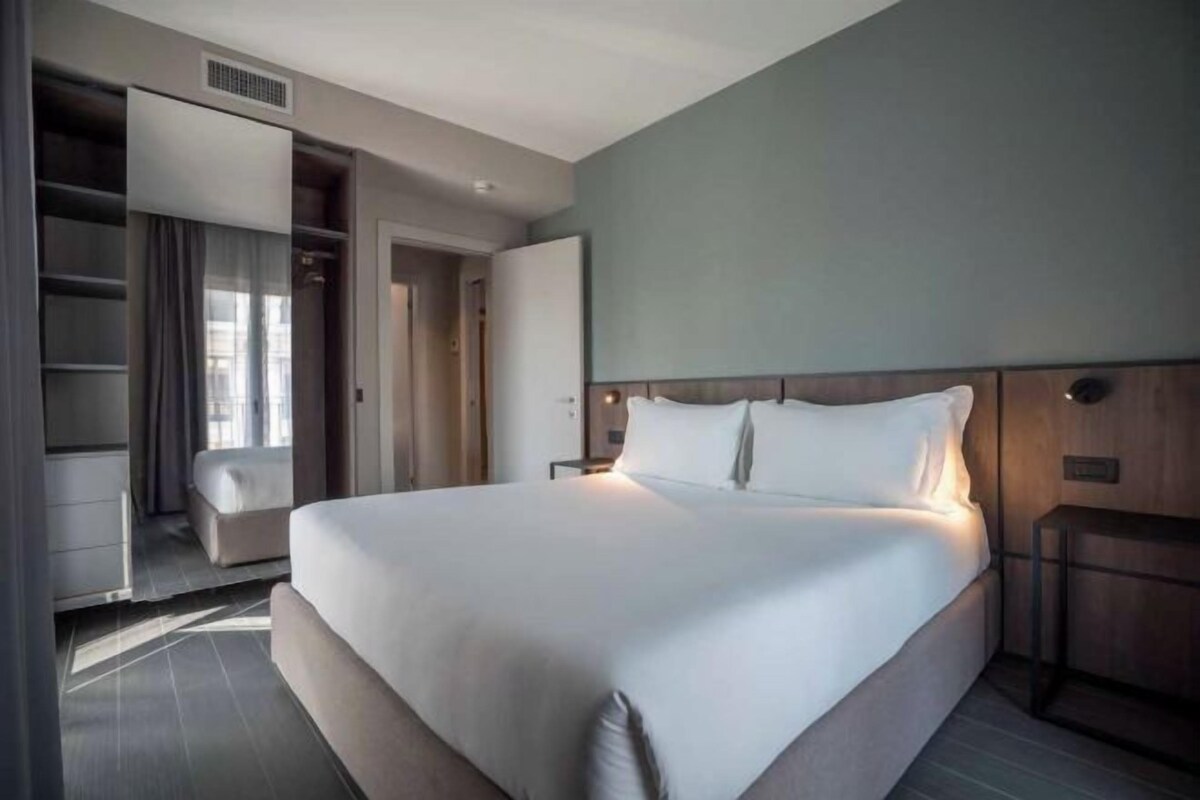 A modern hotel room with a large bed, a walk-in closet, and a view of the city.