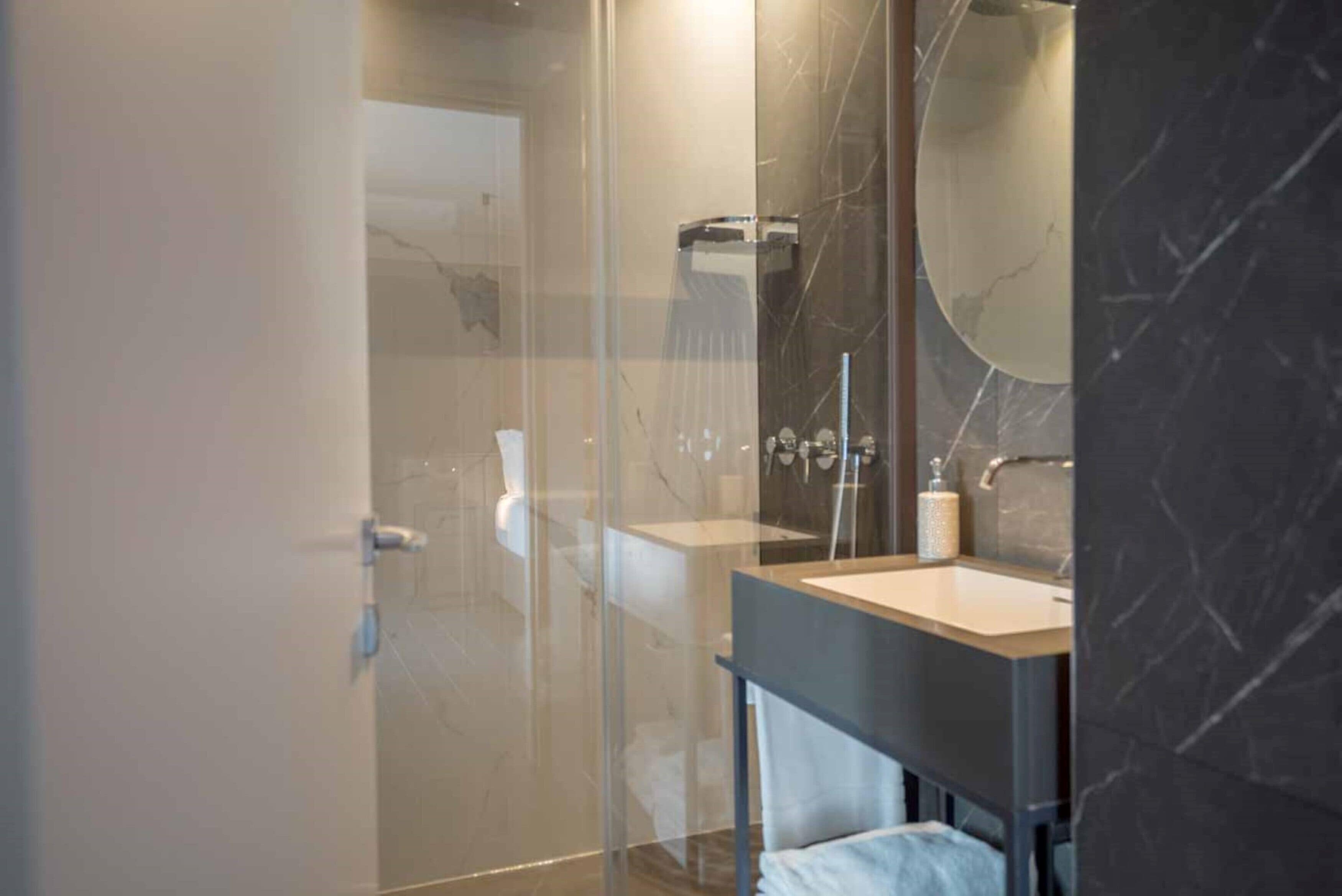 Un baño moderno con cabina de ducha de vidrio, lavamanos de mármol y un espejo grande.