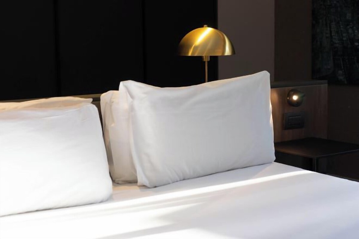 A neatly made bed with white linens and a gold lamp on a bedside table.